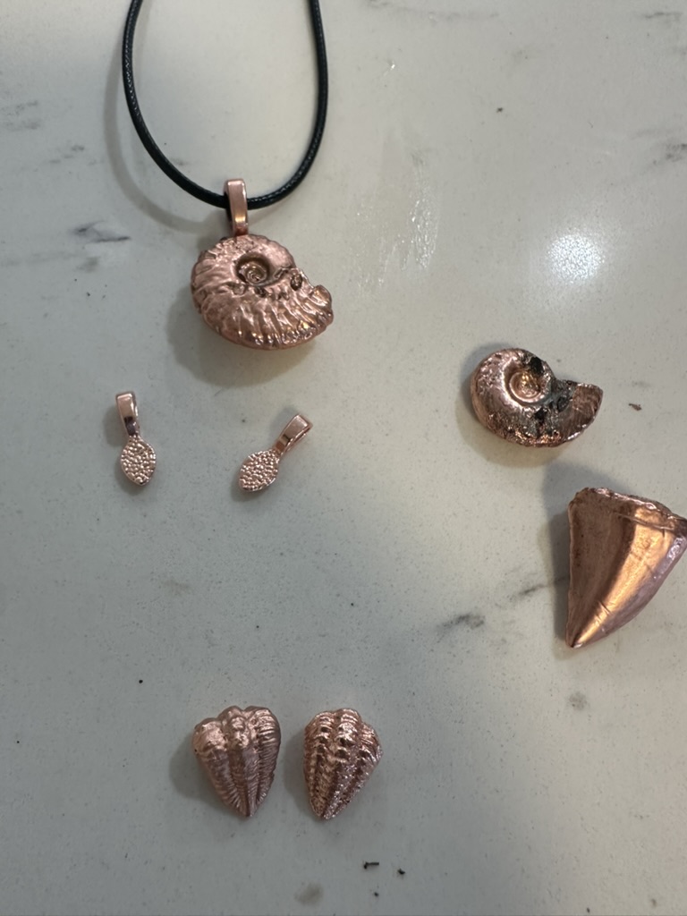 Copper electroformed ammonite pendants, shark tooth, and small shell pieces on marble