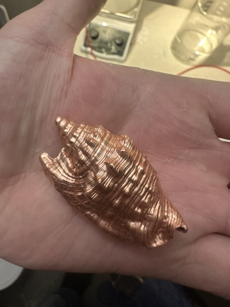 Spiral seashell with a bright copper-colored metallic finish, held in an open palm