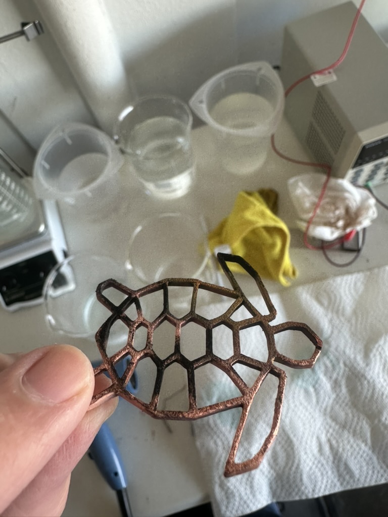 Copper-plated geometric turtle held over a workbench with beakers and plating equipment
