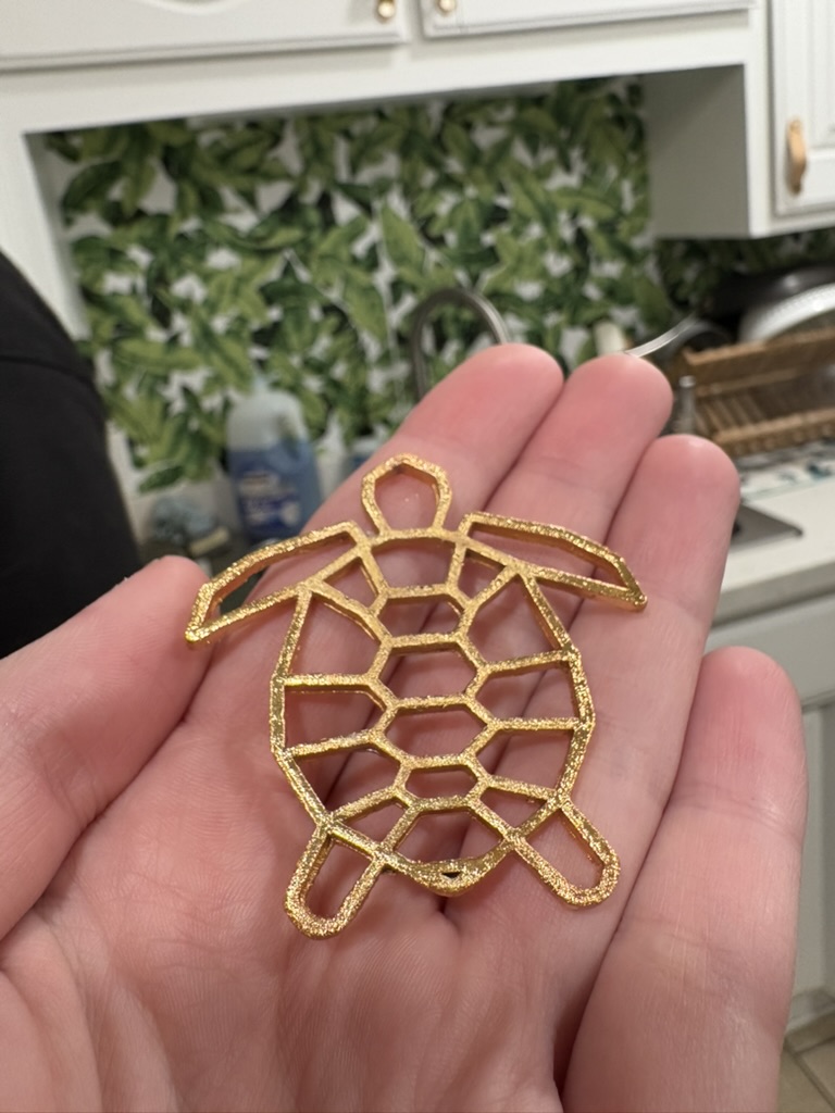 Gold-plated geometric turtle resting in an open palm above a kitchen backsplash