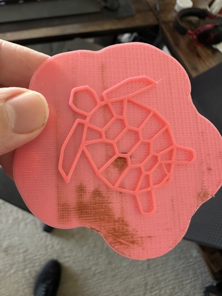 Bright pink 3D-printed geometric sea turtle on a scalloped base, held between fingers